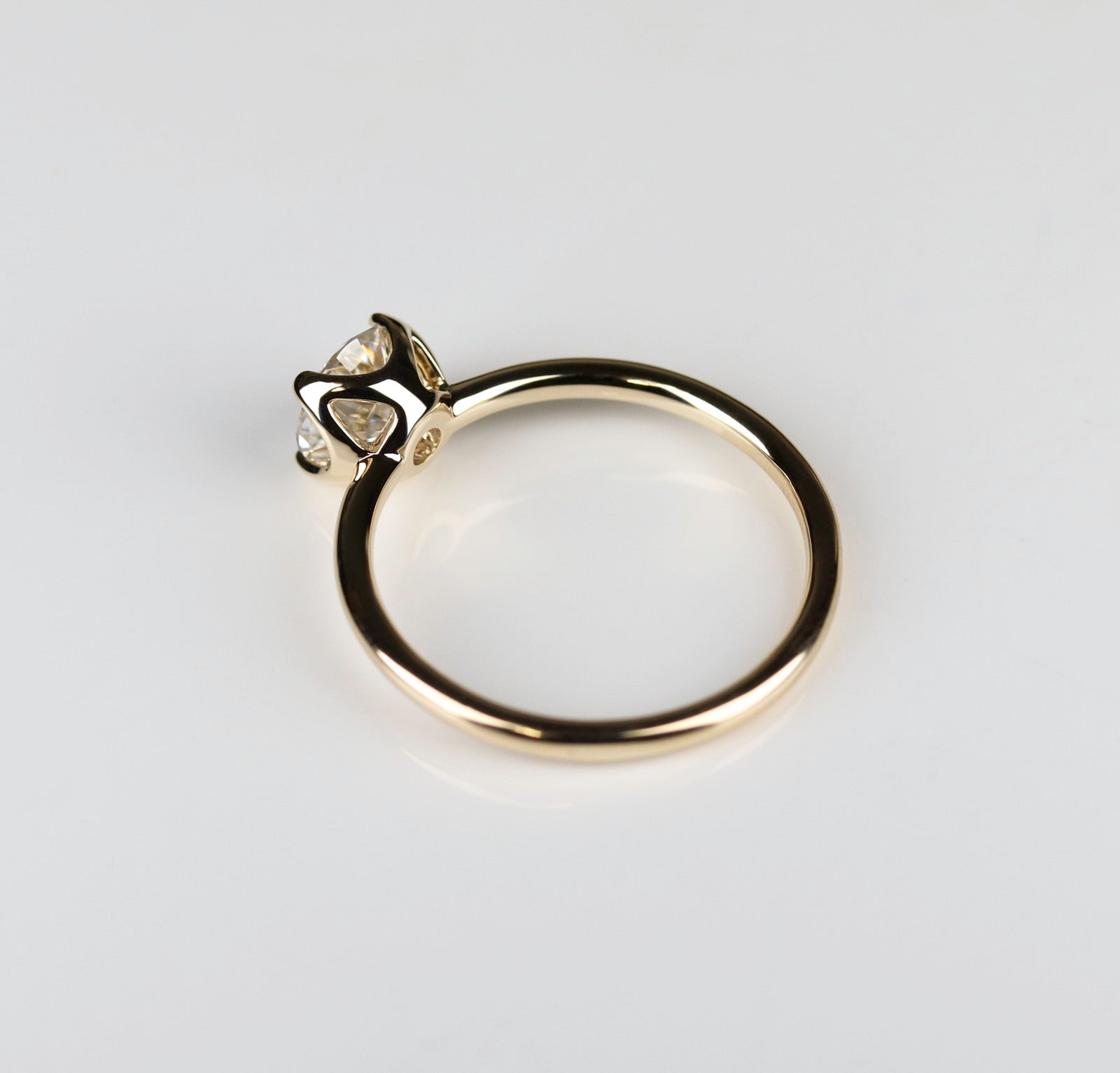Side angle of a yellow gold solitaire engagement ring with a prong-set white moissanite. The center stone is around 6mm in diameter, and is set in a tulip setting.