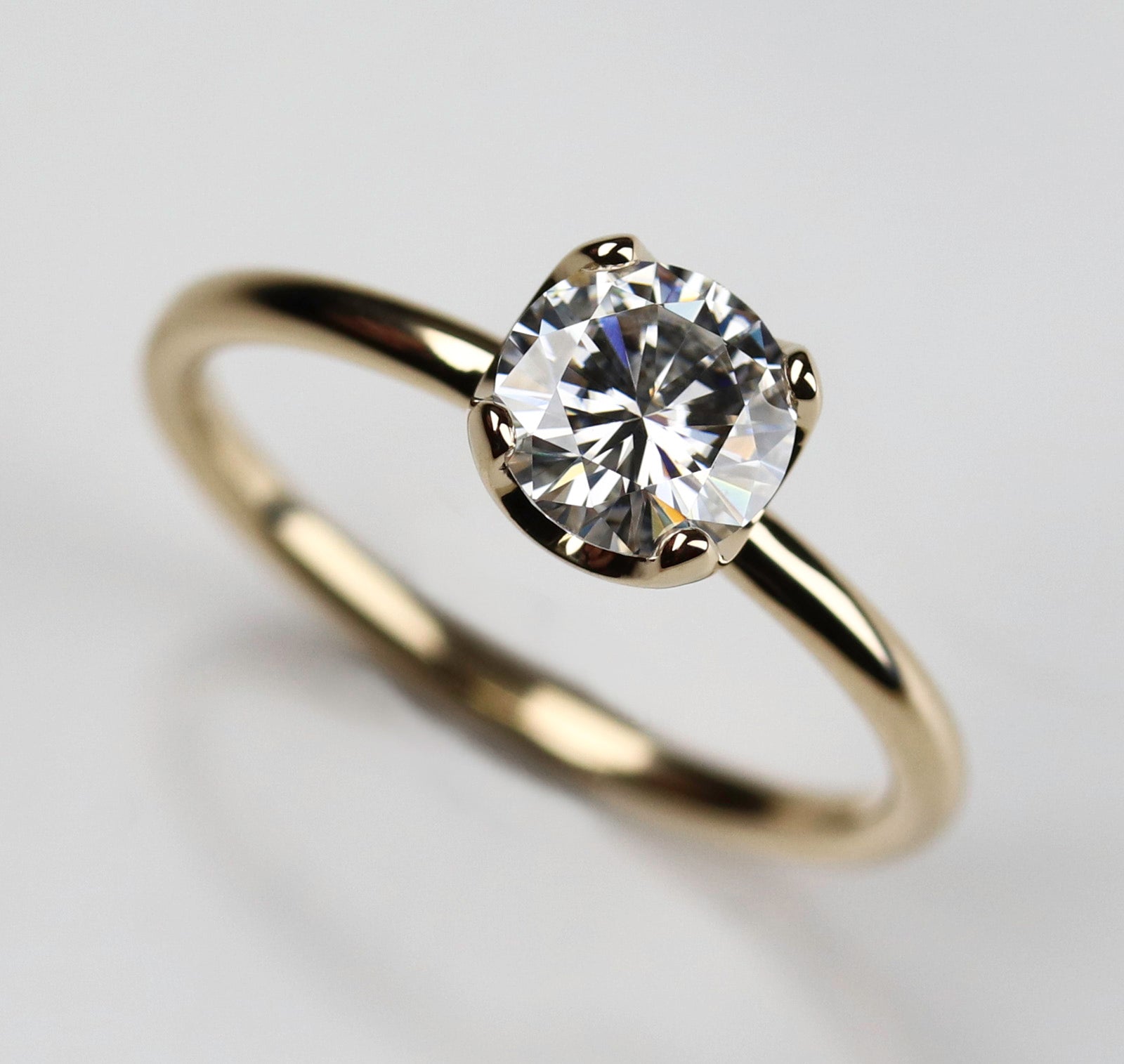 Yellow gold solitaire engagement ring with a prong-set white moissanite. The center stone is around 6mm in diameter, and is set in a tulip setting.