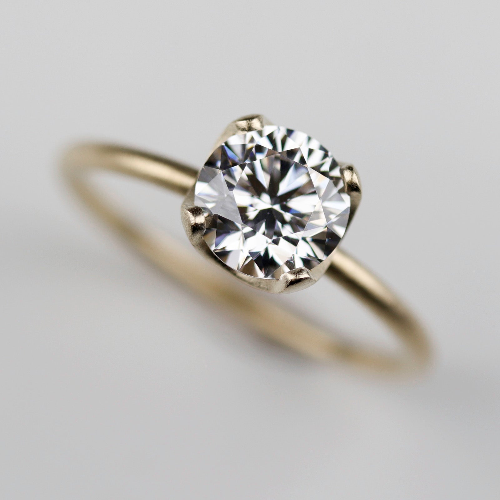 Yellow gold solitaire engagement ring with a prong-set white moissanite. The center stone is around 7mm in diameter, and is set in a tulip setting.