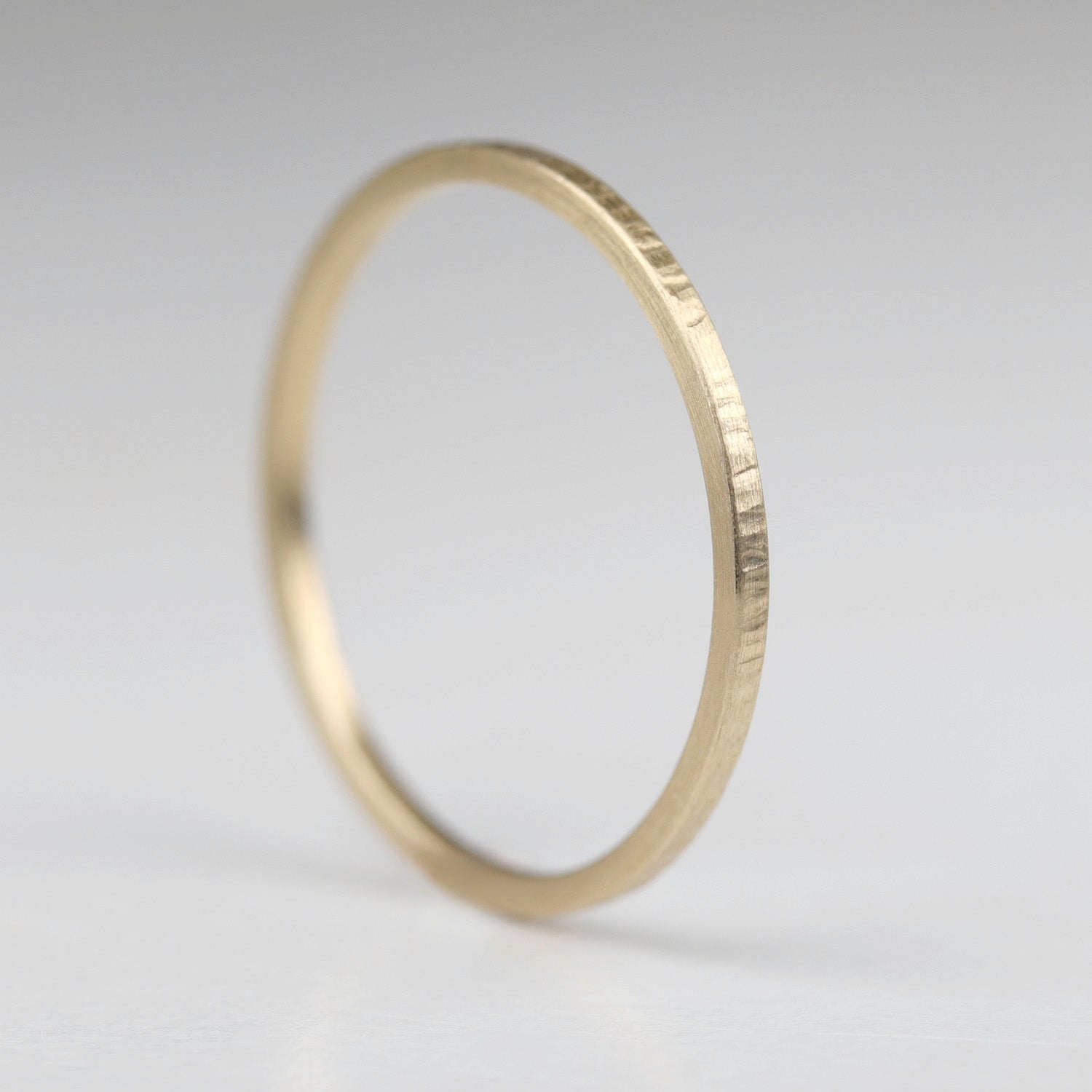A wood textured stacking ring in yellow gold.