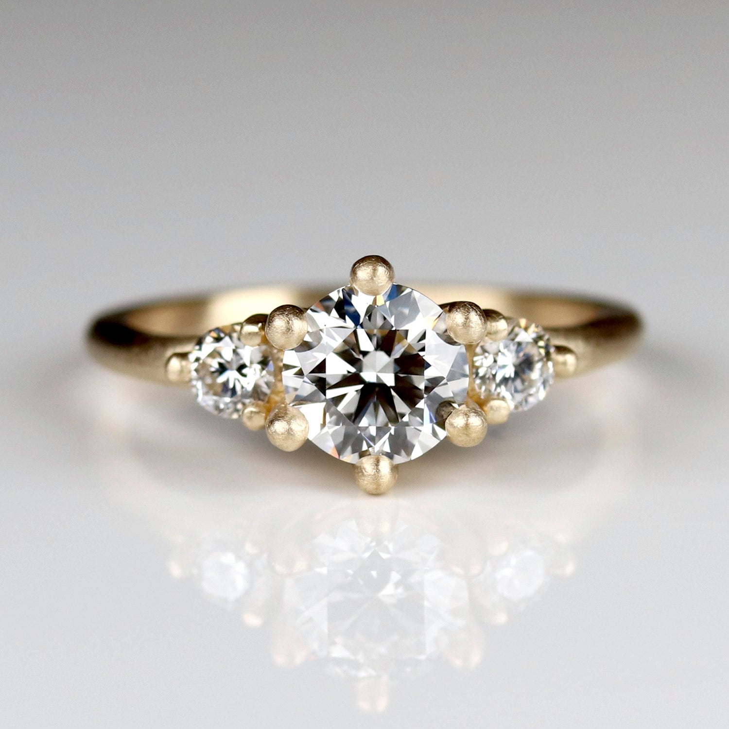A three stone ring style in yellow gold. The center diamond is framed with six prongs, and flanked by two accent diamonds.