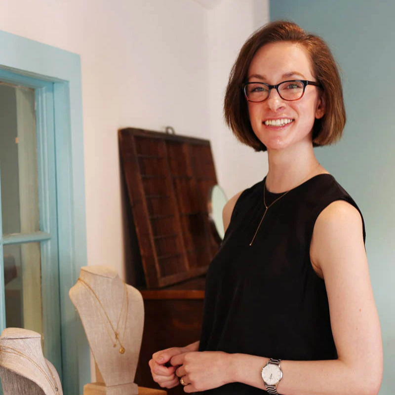 An employee with short hair stands in front of a jewelry display.