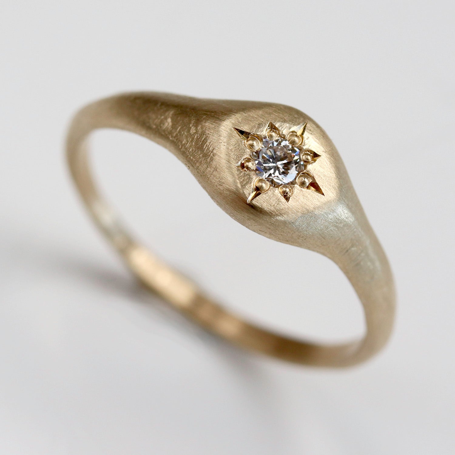 A textured signet ring style in matte yellow gold. The ring is set with a lab diamond in a stylized star shape.