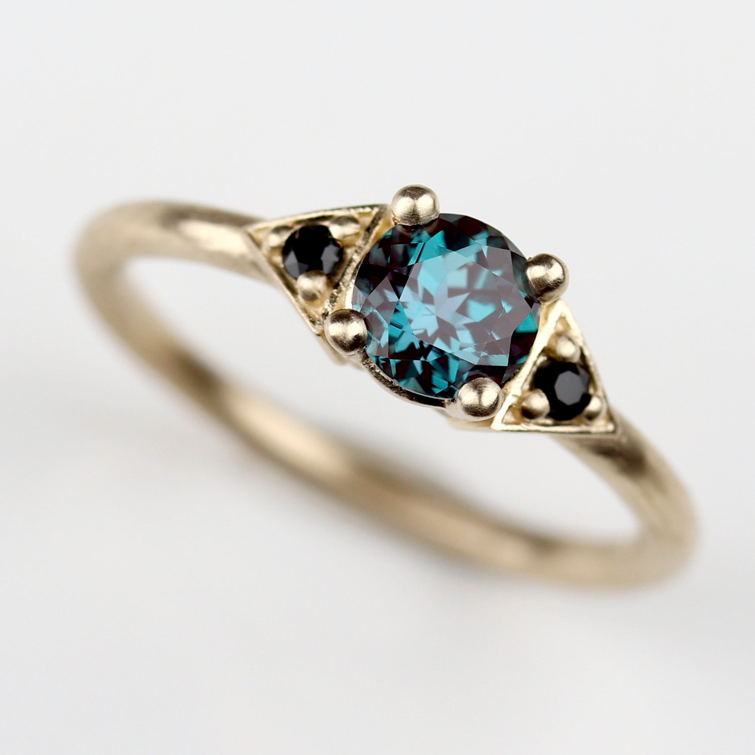 Custom yellow gold engagement ring with an alexandrite center and black spinel accent stones.