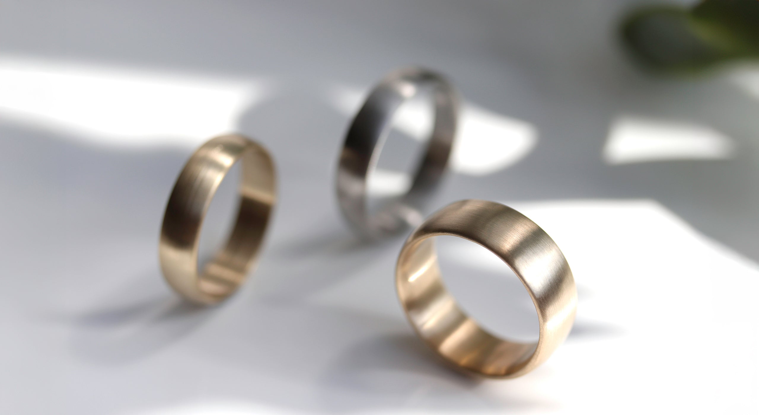 Three core wedding band styles. A classic yellow gold ring sits in the foreground, while the others are slightly out of focus.