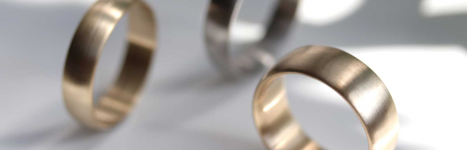 Image of a yellow gold classic wedding band. Two additional rings are out of focus in the background.