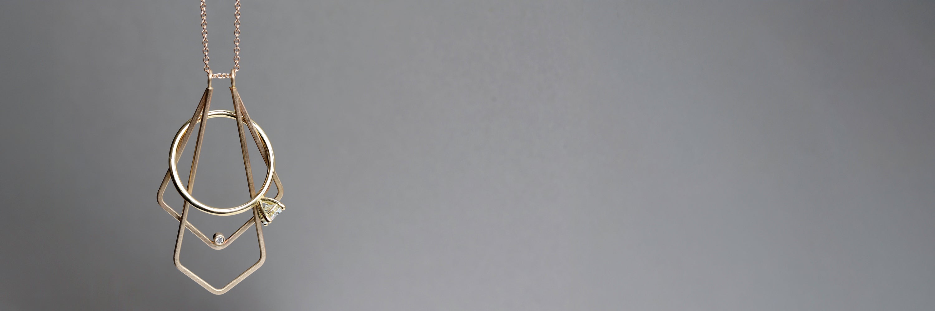 A yellow gold magic ring holder necklace hands against a gray background. The pendant holds a simple solitaire engagement ring.