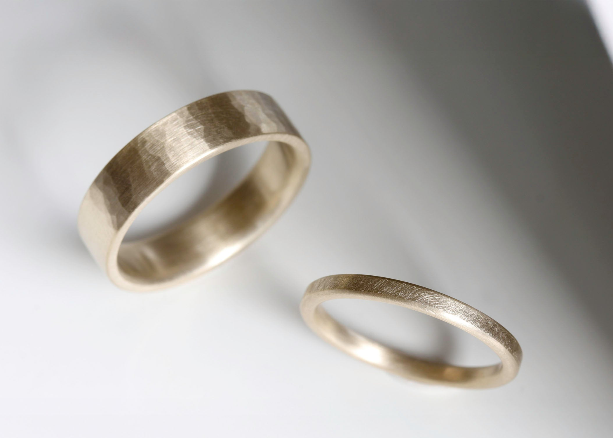A textured wedding band set in matte yellow gold. The wider band has a hammered exterior and the narrower ring has a lightly textured appearance.