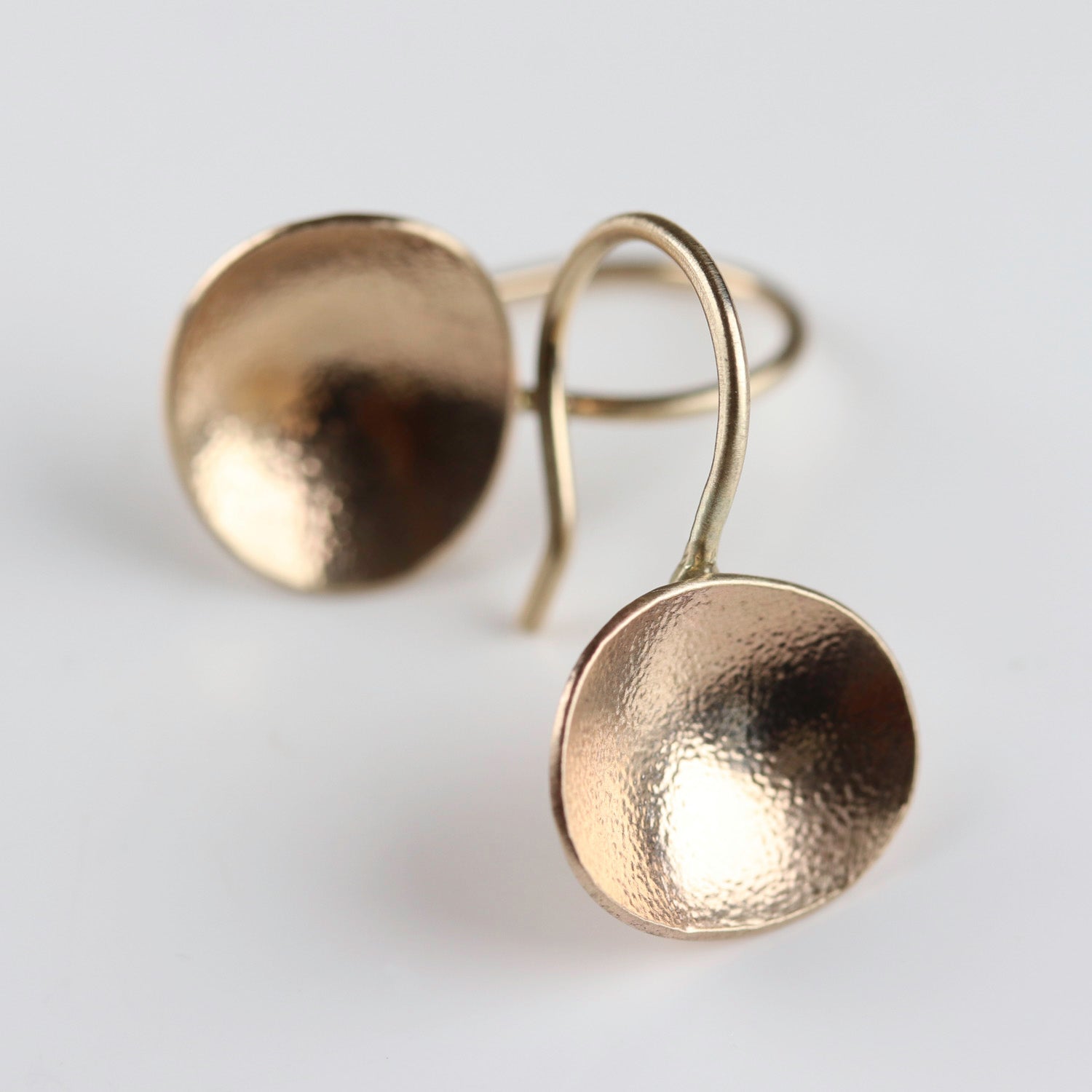 Gold hammer texture dish round dangle earrings on a light gray background