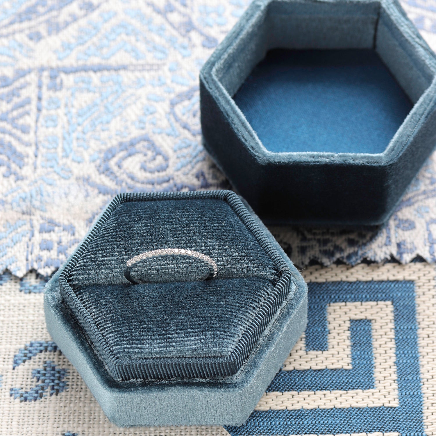 An eternity band sits in a blue velvet hexagon shaped ring box.
