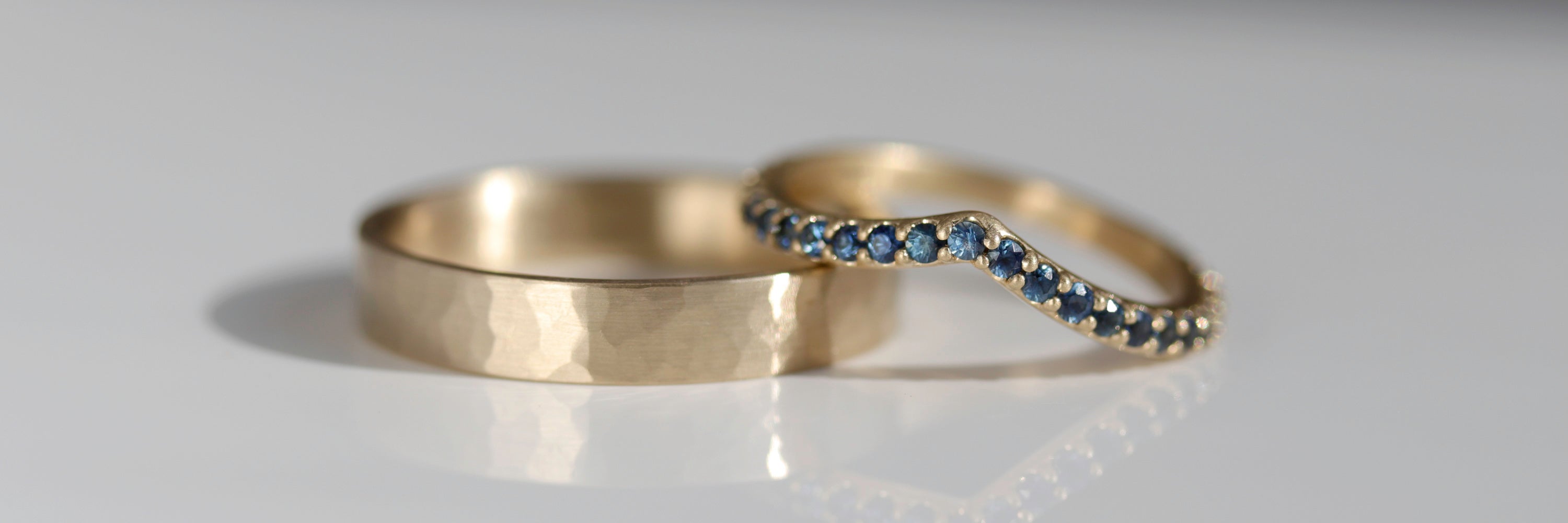 Wedding ring set in matte yellow gold. The flat band has a softly hammer texture surface, while the contour band has blue sapphires.