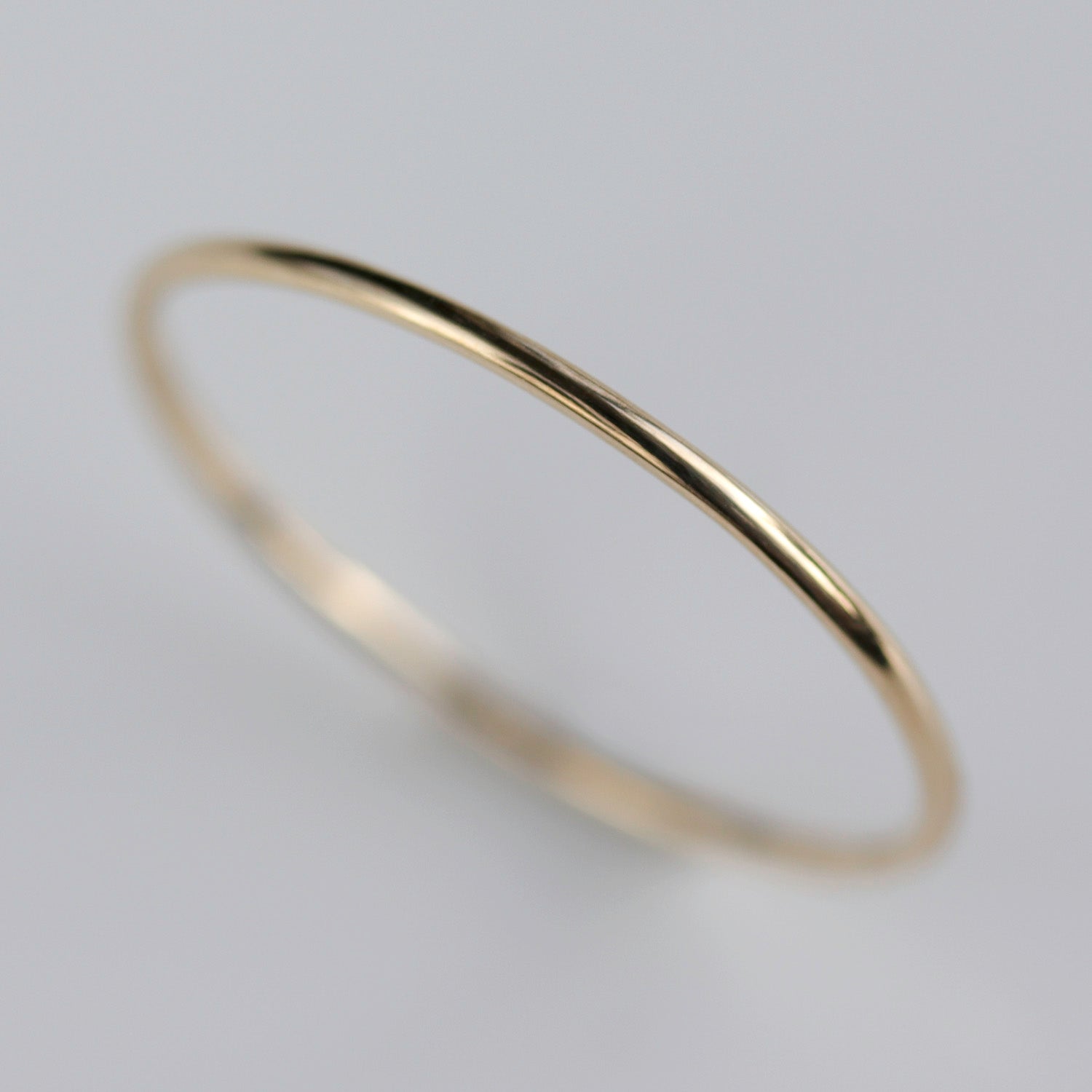 A very narrow stacking ring in shiny 14k yellow gold. The band measures 1mm in diameter and has a round profile.