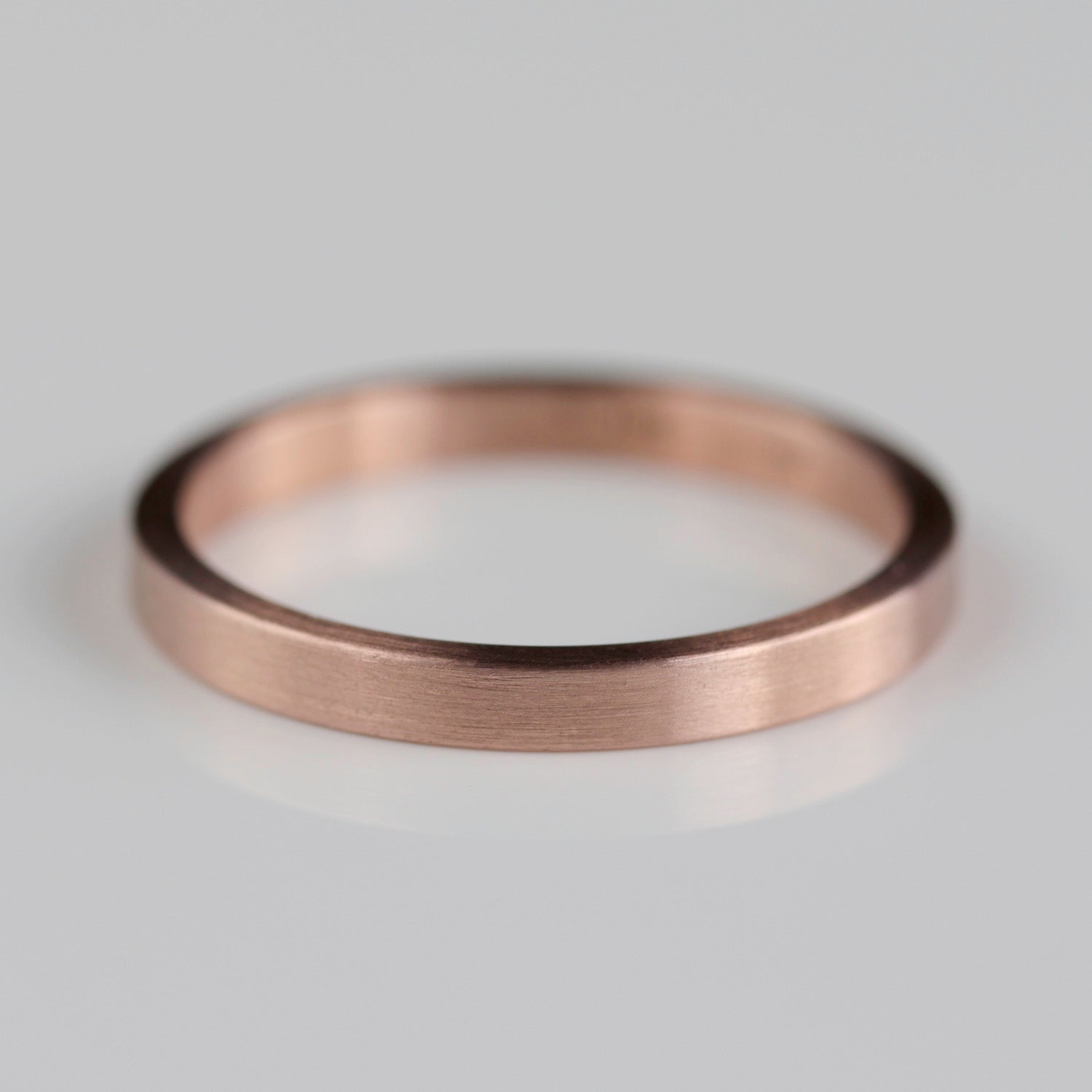 Side angle of a plain smooth women's wedding band style in matte rose gold.