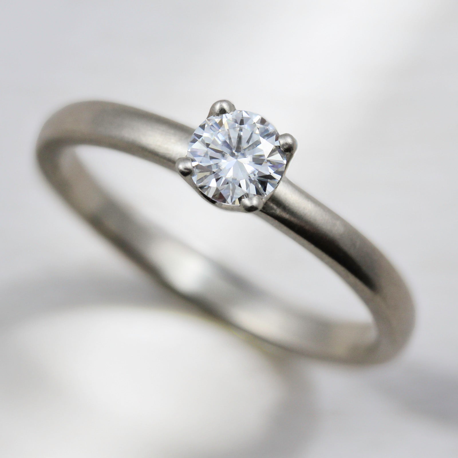 Matte white gold solitaire engagement ring with a prong-set white diamond. The center stone is around 4mm in diameter. 