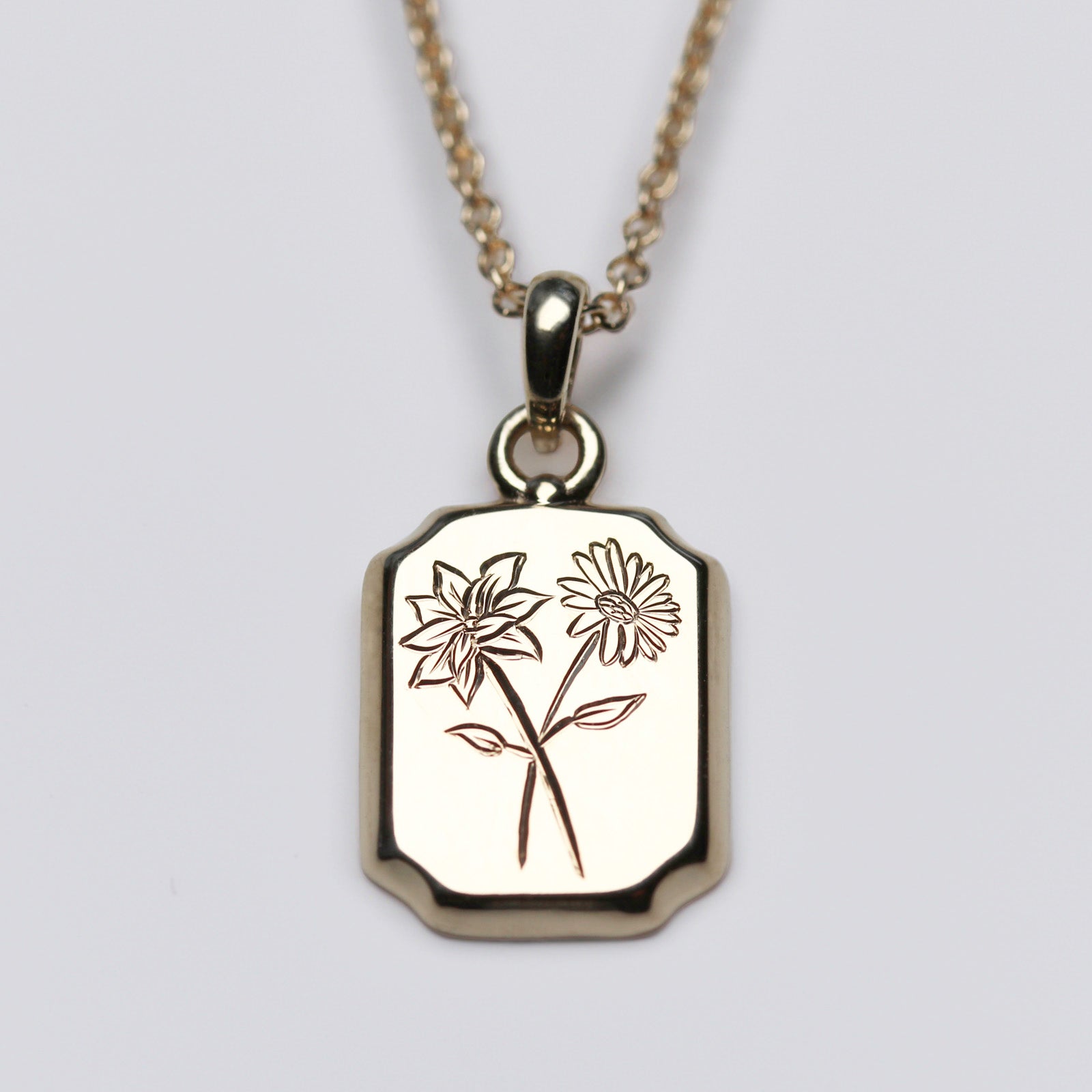 Shiny yellow gold pendant with engraved birth flowers for April and December, daisy and narcissus
