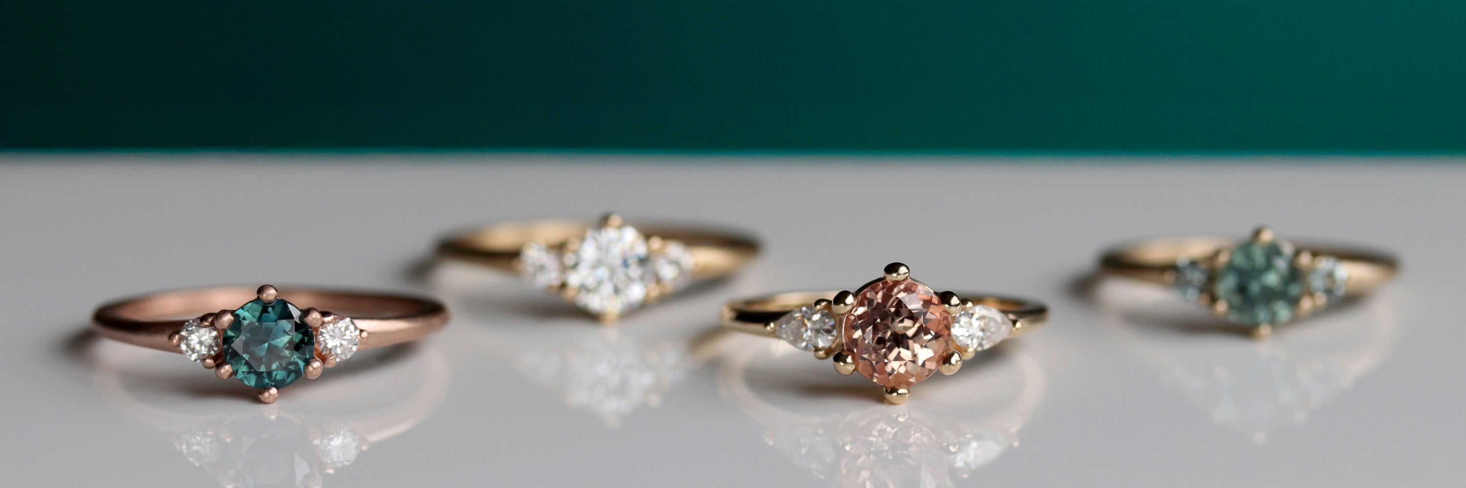 Four three stone engagement rings in rose and yellow golds, showing different color combos and center stone colors.