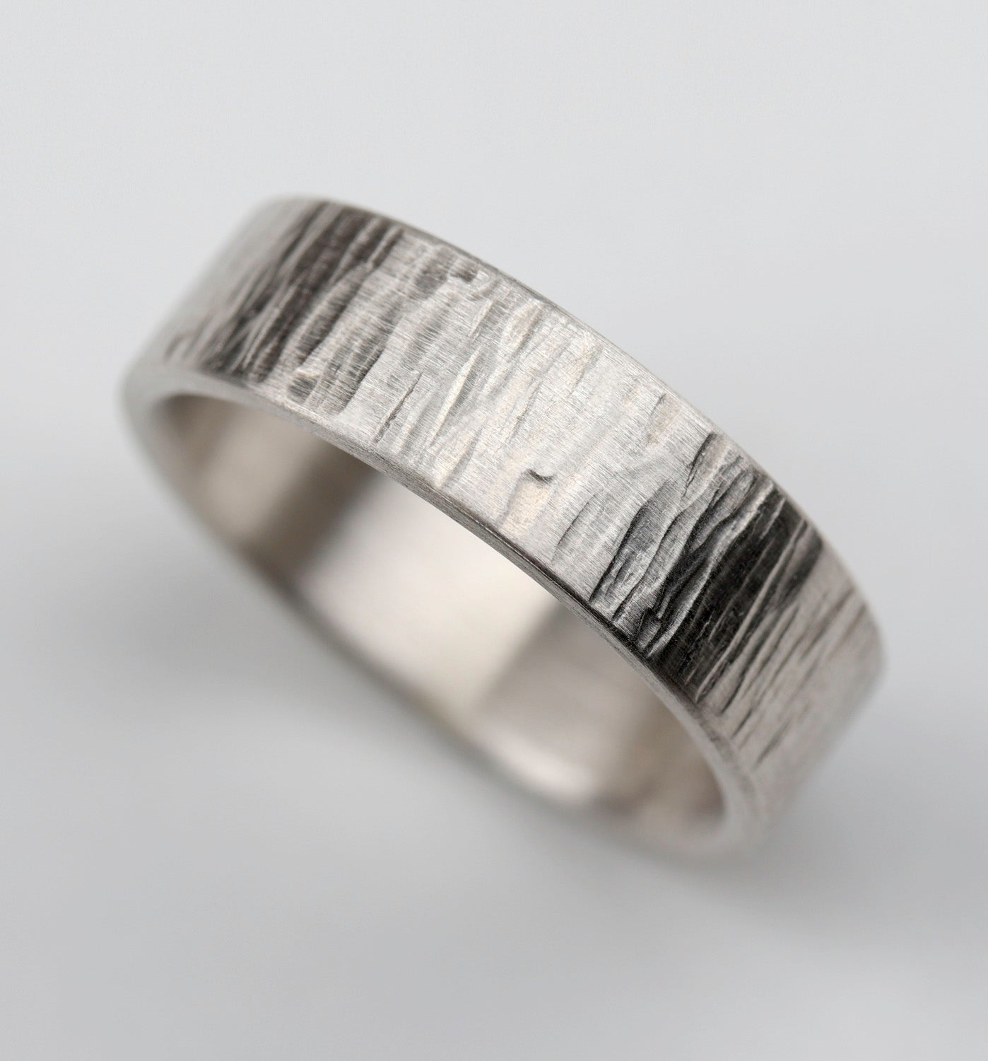 A wood textured sterling silver men's engagement ring. The surface is textured with a matte finish.