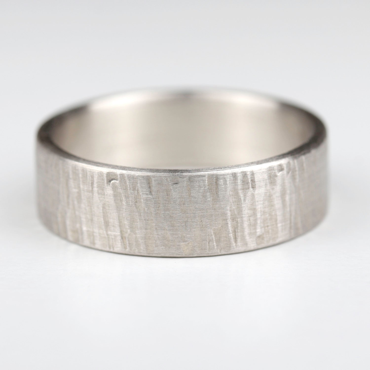 A wood textured sterling silver men's engagement ring. The surface is textured with a matte finish.