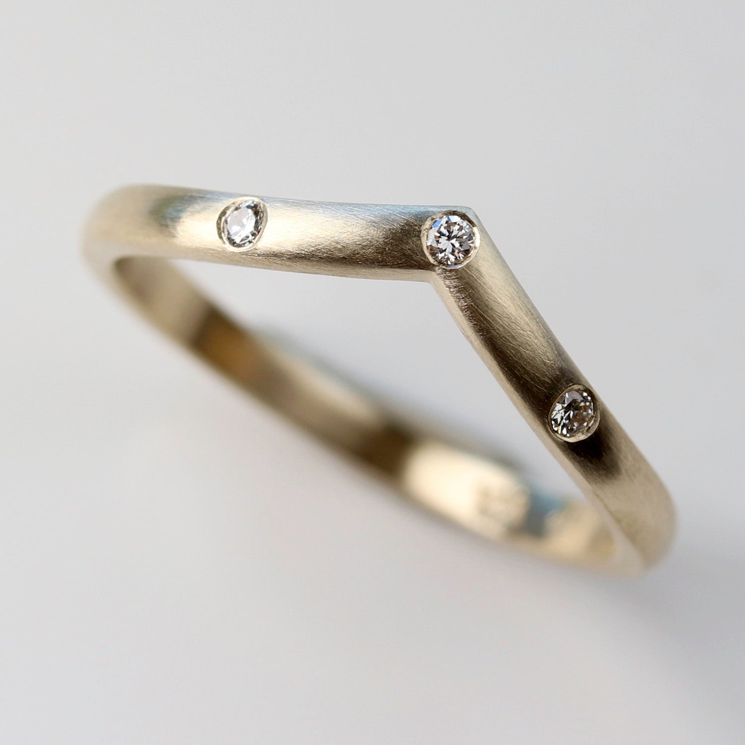 A contoured wedding band style with three flush set diamonds. The band has a v-shaped contour and a matte finish.