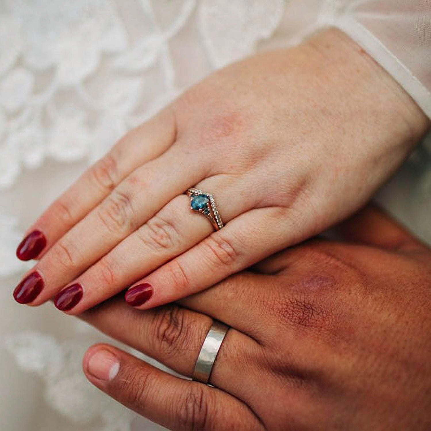A couple wearing their wedding bands. One wearing a rose gold and sapphire three stone ring with a pave contour band, the other wears a matte hammer texture wedding band.
