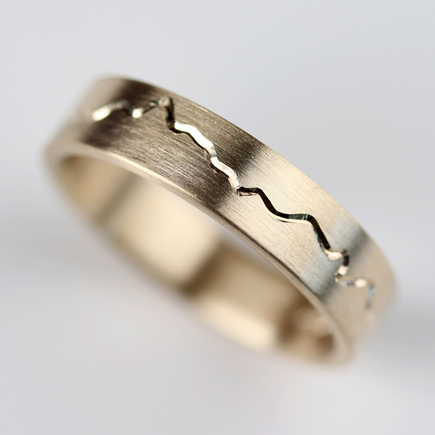 Gold ring with engraved design on a light gray background